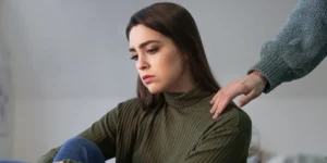 صورة فتاة حزينة تجلس مع نفسها، وأحد أصدقائها يربت على كتفها لمواساتها. تعكس الصورة مشاعر الحزن التي تسيطر على الضحية عندما تنفصل عن النرجسي.