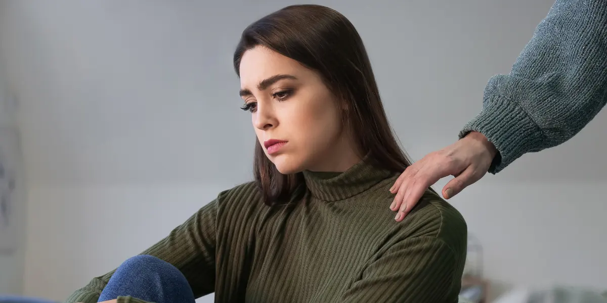 صورة فتاة حزينة تجلس مع نفسها، وأحد أصدقائها يربت على كتفها لمواساتها. تعكس الصورة مشاعر الحزن التي تسيطر على الضحية عندما تنفصل عن النرجسي.